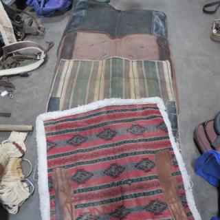 Assorted saddle blankets with striped and geometric patterns, showing slight wear. Includes leather accents and fleece lining.