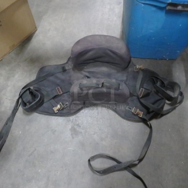 Black saddle with attached bags, showing signs of wear. Features adjustable straps and metal buckles, suitable for horseback use.