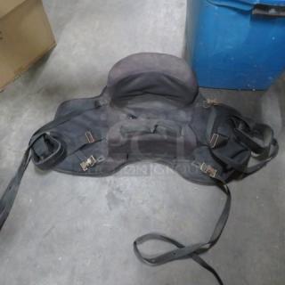 Black saddle with attached bags, showing signs of wear. Features adjustable straps and metal buckles, suitable for horseback use.