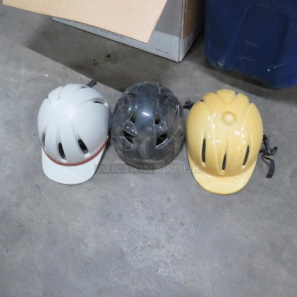 Assorted riding hats in white, black, and yellow. Used condition, visible scuffs, with ventilation slots. Suitable for biking.