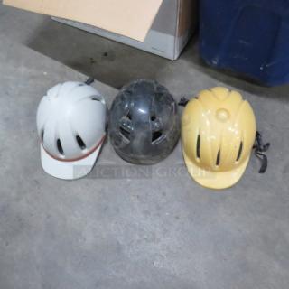 Assorted riding hats in white, black, and yellow. Used condition, visible scuffs, with ventilation slots. Suitable for biking.