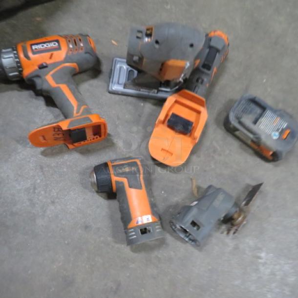 Assorted Rigid power tools on concrete, including a drill, sander, flashlight, and battery. Signs of wear visible.