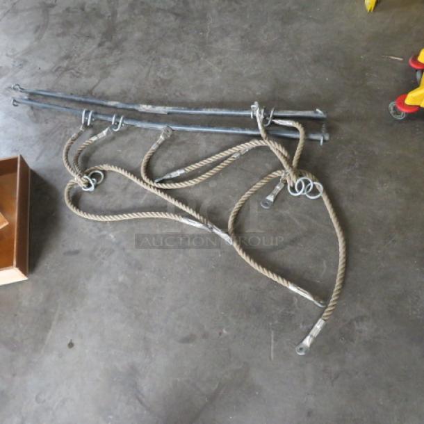 Assorted hardware bundle with metal rods and coiled ropes, featuring metal hooks. Used condition on concrete floor.