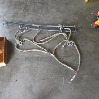 Assorted hardware bundle with metal rods and coiled ropes, featuring metal hooks. Used condition on concrete floor.