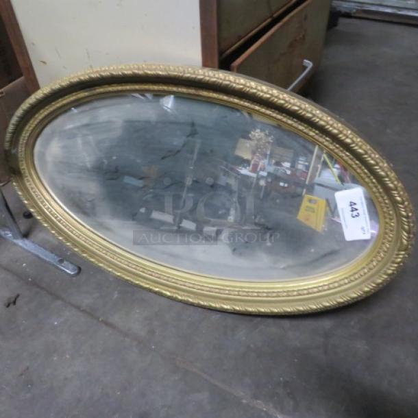 Oval gold-framed mirror with intricate detailing, moderate wear. Auction tag "443" attached.