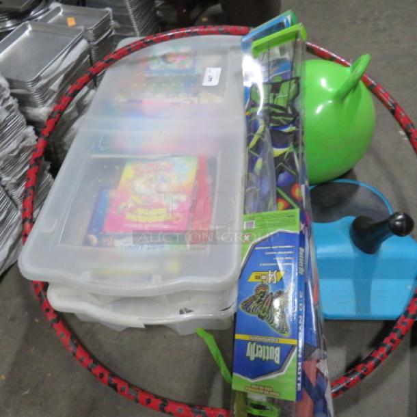 Assorted lot including large hula hoop, green bouncy ball, plastic storage boxes with games, blue toy base, and packaged toy set.