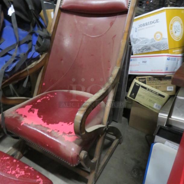 Vintage leather chair with ottoman, showing wear on the red leather. Curved wooden arms, visible in a cluttered room.