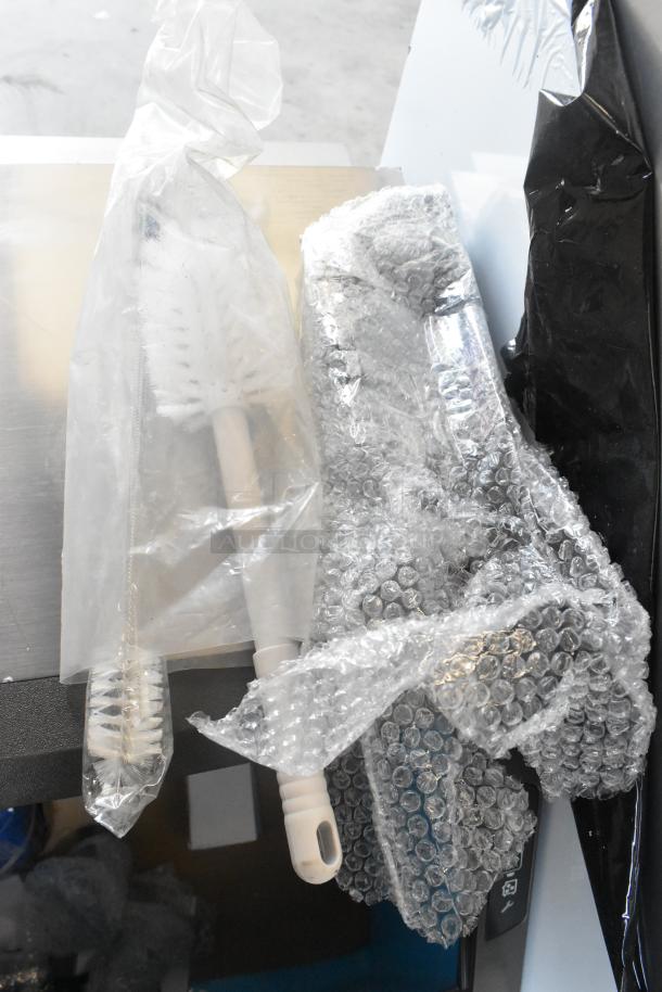 Wrapped accessories for the 2024 Manitowoc UDF0240A-161B ice machine, including a cleaning brush in protective packaging.