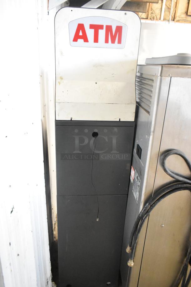 Hyosung metal floor ATM, used condition, visible ATM signage, sturdy black base, located in narrow space.