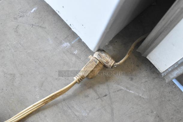 R-54SC Metal Commercial 2 Door Reach In Cooler power cord on concrete floor, showing wear and usage marks.
