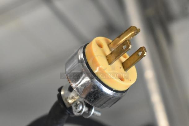 Close-up of a three-prong electrical plug with a metallic casing, showing wear, likely belonging to a commercial appliance.