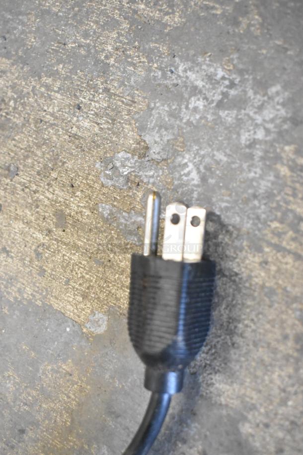 A close-up of a black three-prong electrical plug on a textured concrete surface.