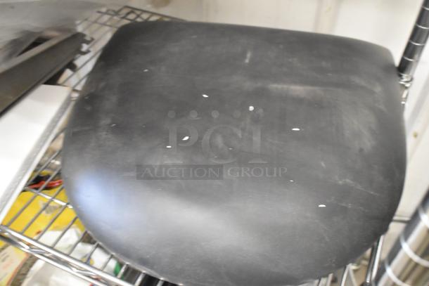 Alt text: Black cushion on metal shelving, next to metal brackets, showing slight wear. Part of auction lot with various items.