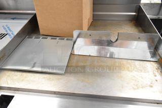 Box of assorted metal pieces, including slotted and curved metal sheets on a metal surface, good condition.