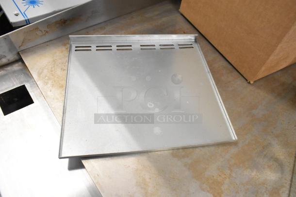 Box of metal pieces showing a square metal sheet with vent-like slots and light marks. Ideal for crafting or repairs.