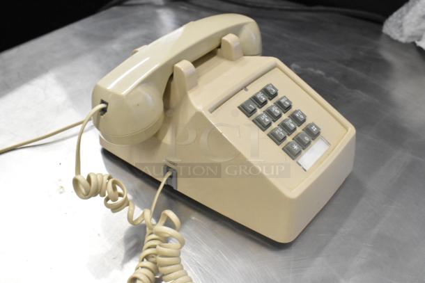 Vintage beige corded telephone with push-button dial on stainless steel surface. Features curly cord and handset port.