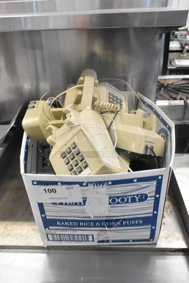 Box of vintage beige corded telephones, multiple units with numeric keypads, in used condition, in a cardboard box.