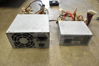 AT-265SFX power supplies on a concrete floor, featuring visible wires and connectors, in used condition.
