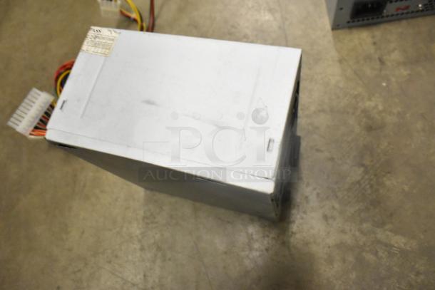 AT-265SFX power supply, silver casing, visible cables, label with specifications, slight wear on metal surface.