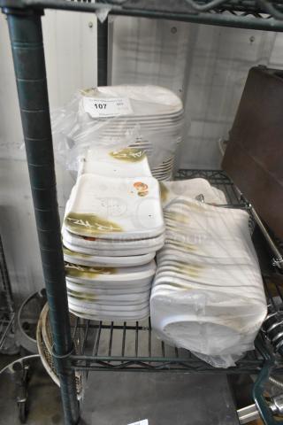 Lot of rectangular white dishes with decorative green and orange design, stacked on a shelf. Auction label reads "107 QTY 1-4."