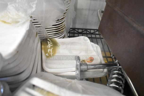 Lot of various dishes on a rack, featuring square plates with floral designs. Some plates have visible residue. Condition appears used.