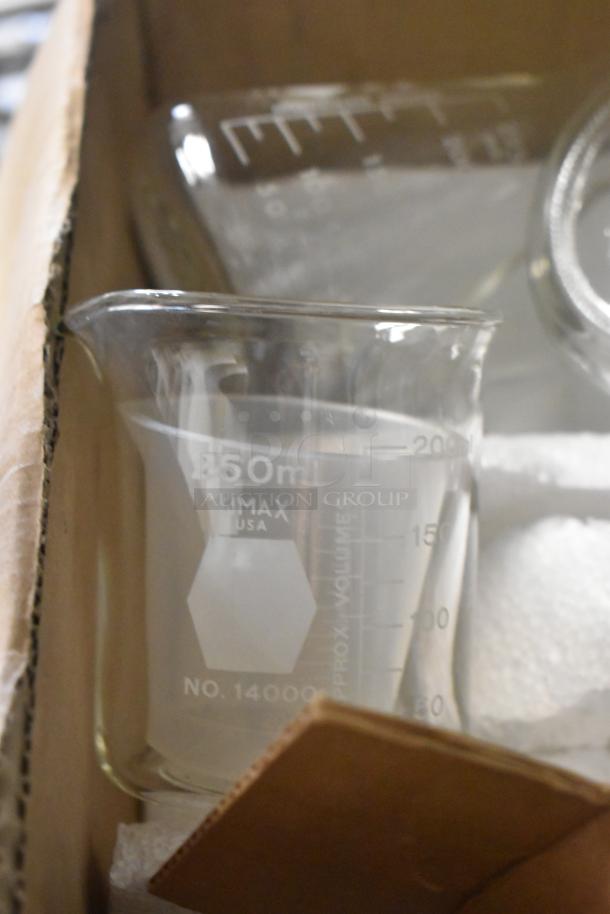 Glass beaker labeled "250 ml, Kimax, USA" in a box. Surrounded by other lab glassware.
