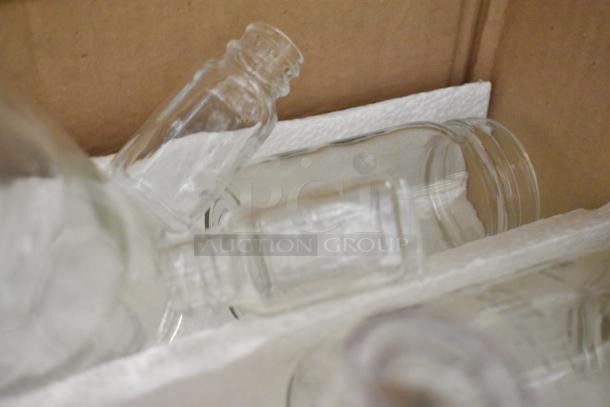 Lot of various clear glass bottles in a cardboard box with foam padding, items including a booster seat and spray nozzle attachment not visible.