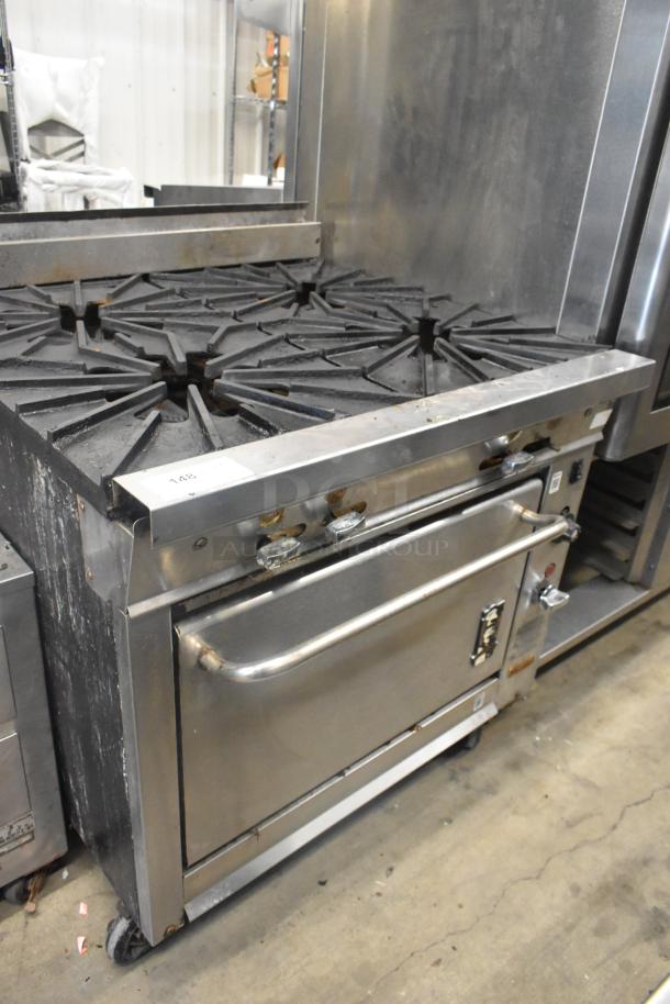 Montague stainless steel commercial gas range with 4 burners, oven, and commercial casters. Visible wear, suitable for kitchen use.