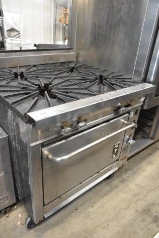 Montague stainless steel commercial gas range with 4 burners, oven, and commercial casters. Visible wear, suitable for kitchen use.