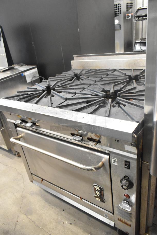 Montague Stainless Steel Commercial 4 Burner Gas Range with Oven on Casters; shows signs of use, control knobs visible.