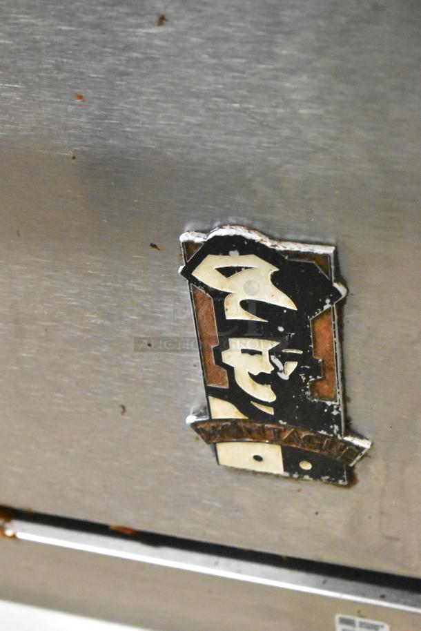 Montague stainless steel commercial gas range with 4 burners and oven, on commercial casters. Visible worn Montague logo.