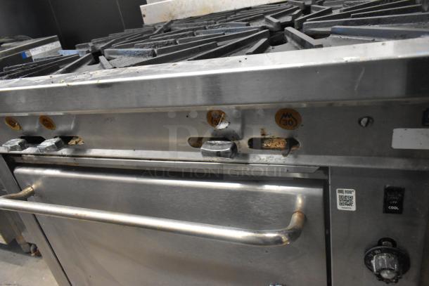 Montague stainless steel commercial gas 4-burner range with oven, worn condition, features control knobs and commercial casters.