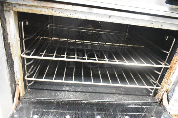 Montague stainless steel 4-burner gas range oven, commercial-grade, mounted on casters, visible signs of use.