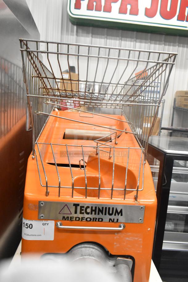 Metal commercial floor citrus juicer on casters, 115 volts, 1 phase, "Technium Medford NJ" label, orange body, wire basket.