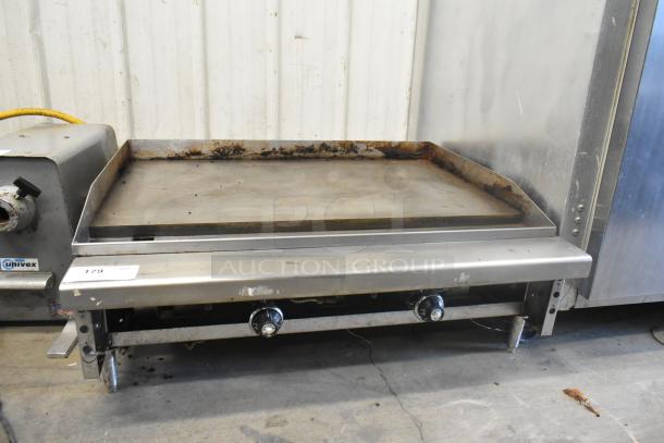 Stainless steel commercial gas-powered countertop griddle with flat top, two control knobs, showing signs of use.