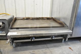 Stainless steel commercial gas-powered countertop griddle with flat top, two control knobs, showing signs of use.