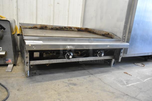 Stainless steel commercial countertop gas griddle, flat top, visible wear, dual control knobs, sturdy legs, used condition.