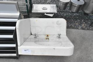 Wall-mounted single bay sink with dual faucets, features visible rust and wear marks, auction tag attached.