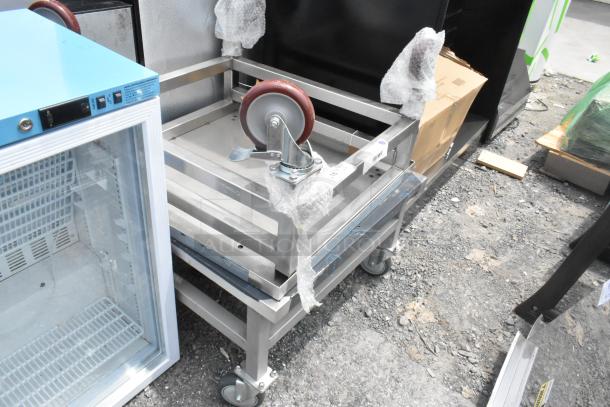 2 stainless steel equipment stands on commercial casters, excellent condition, with protective bubble wrap and visible markings.