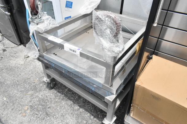 2 stainless steel equipment stands on commercial casters, new condition, with protective wrap. Labels indicate batch numbers.