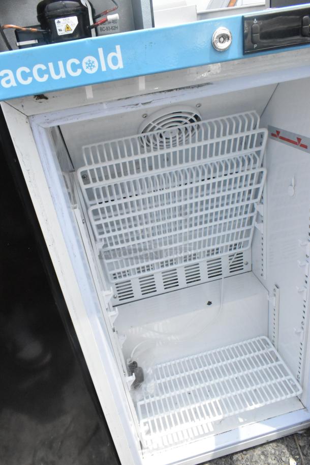 Open AccuCold mini cooler, metal shelves, white interior, visible fan and compressor, 120V, 1 phase, lightly used.