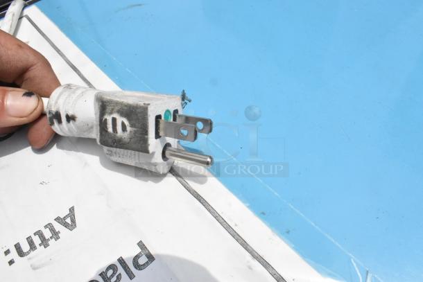 A white electrical plug with visible signs of use, including dirt and wear, on a light blue surface.