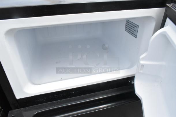 Open mini cooler interior, showing spacious white compartment and door with caution label, model unspecified.