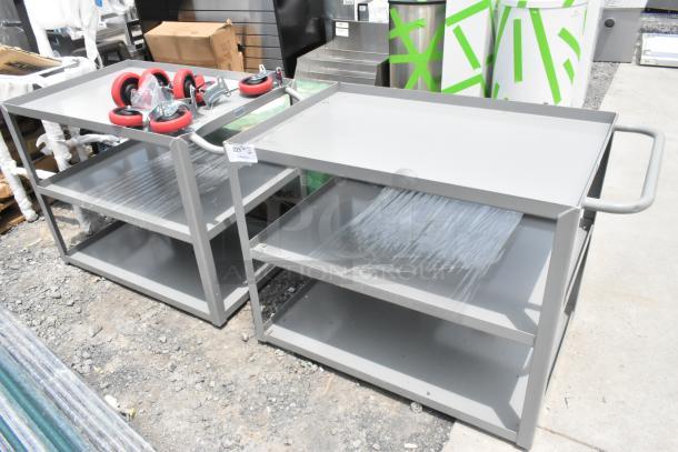 Two brand new gray metal 3-tier carts, scratch and dent condition. Includes red casters and plastic wrap protection.