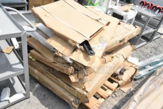 Stack of eight brand new scratch and dent items, including tables and table bases, in damaged cardboard packaging on a pallet.