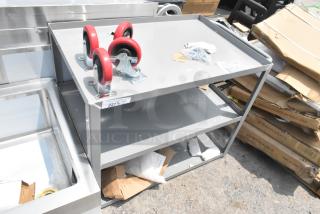 Gray metal 3-tier cart with red commercial casters, scratch and dent condition, brand new parts, visible tags and fixtures.