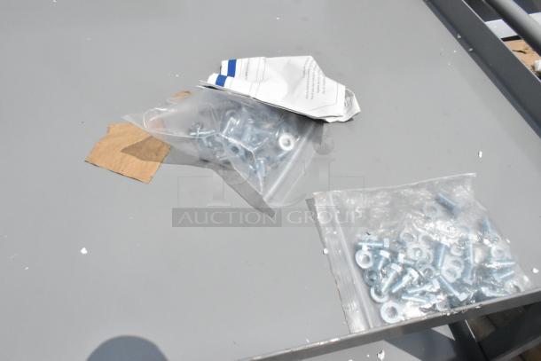 Gray metal 3-tier cart assembly components; includes screws and washers in plastic bags. Minor scratches visible.