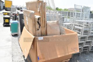 Large cardboard box containing scratch and dent tabletops, stainless steel tables, and Metro shelves. Visible wear on packaging.