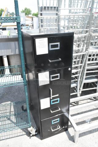 Black metal 4-drawer filing cabinet with labels for organizing. Slight wear visible. Ideal for office storage.