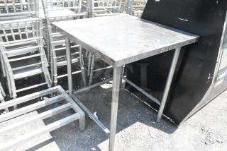 Stainless steel table with square top, sturdy legs, and slightly worn surface. Ideal for industrial or kitchen use.
